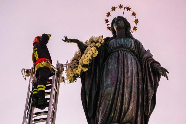 Firefighter places wreath on a statue of Mary.