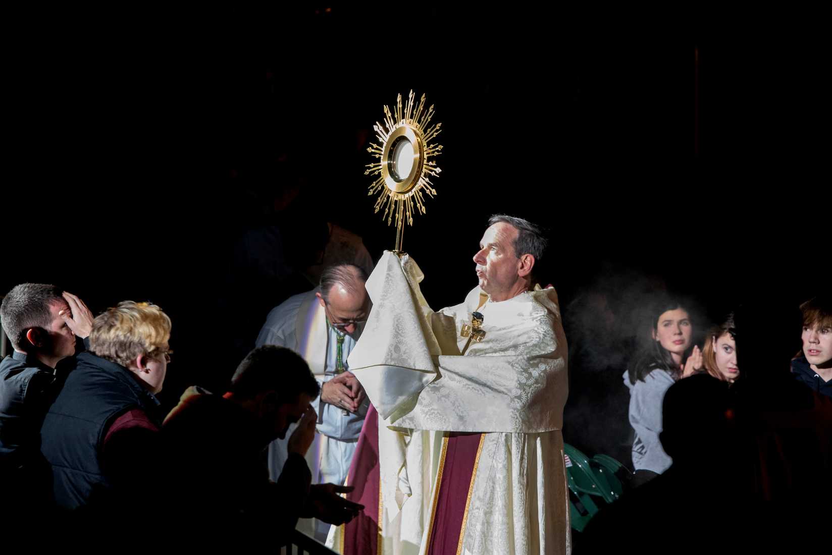 Bishop Burbidge holds the monstrance during a Eucharistic procession while people bow their heads in prayer around him