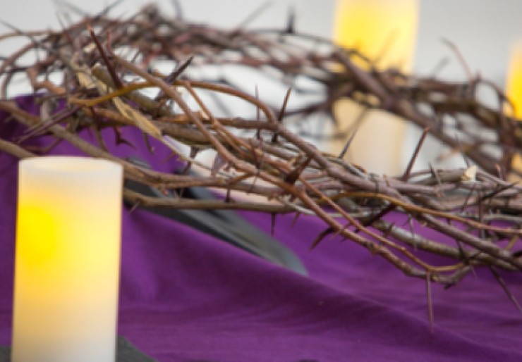 crown of thorns on purple cloth with pillar candles in close foreground and background behind crown of thorns